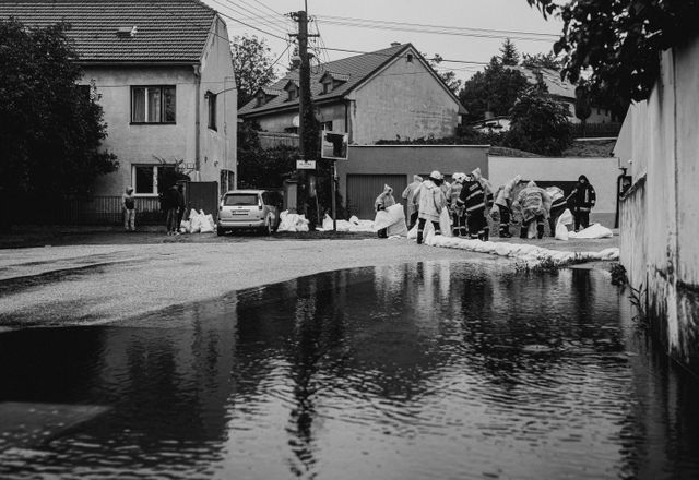 Crews in rain gear building sandbag barriers in a flooded street