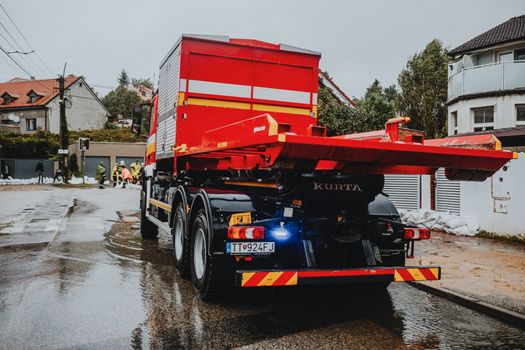 A red tow truck parked on a wet street in an urban neighborhood with workers in the background.