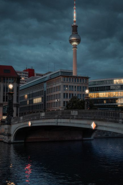 Serene twilight view of Berlin TV Tower overlooking a river and bridge, emphasizing urban architecture.