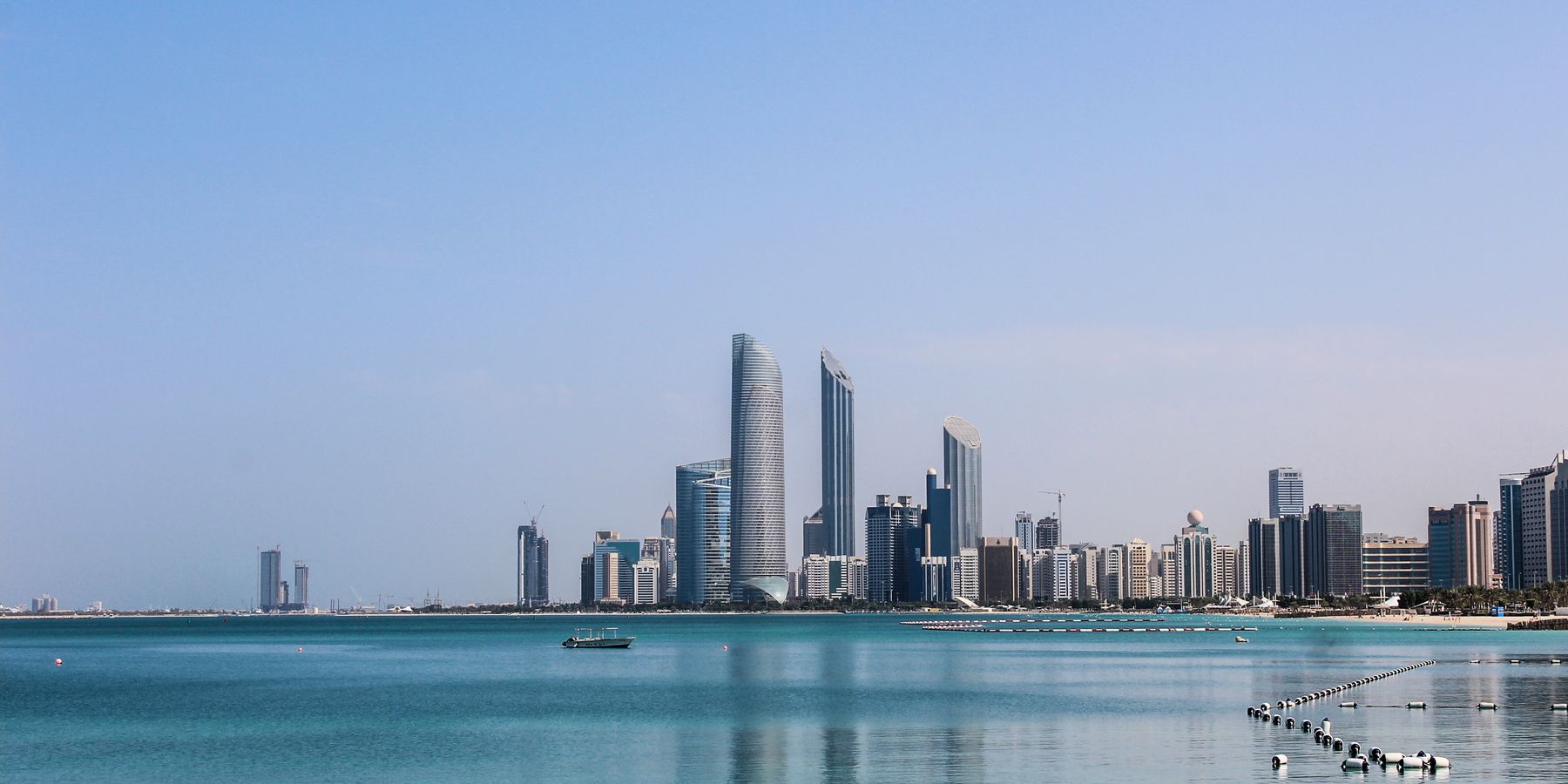 Stunning view of the Abu Dhabi skyline reflecting in the calm Gulf waters on a sunny day.