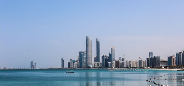 Stunning view of the Abu Dhabi skyline reflecting in the calm Gulf waters on a sunny day.