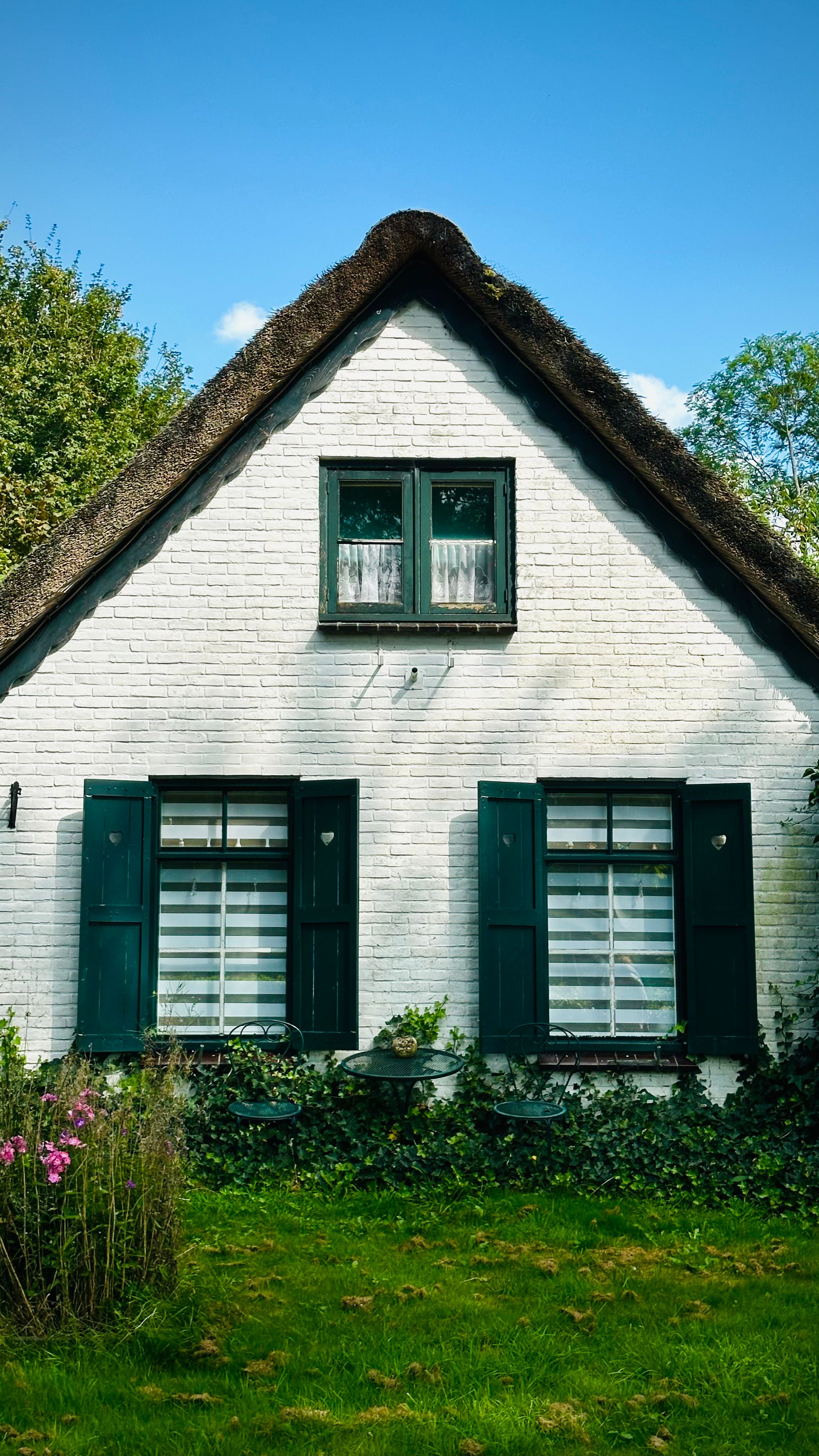 Pittoresk wit huisje met een rieten dak en weelderige groene omgeving.