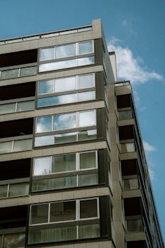 Upward view of a modern high-rise building with large windows against a blue sky.