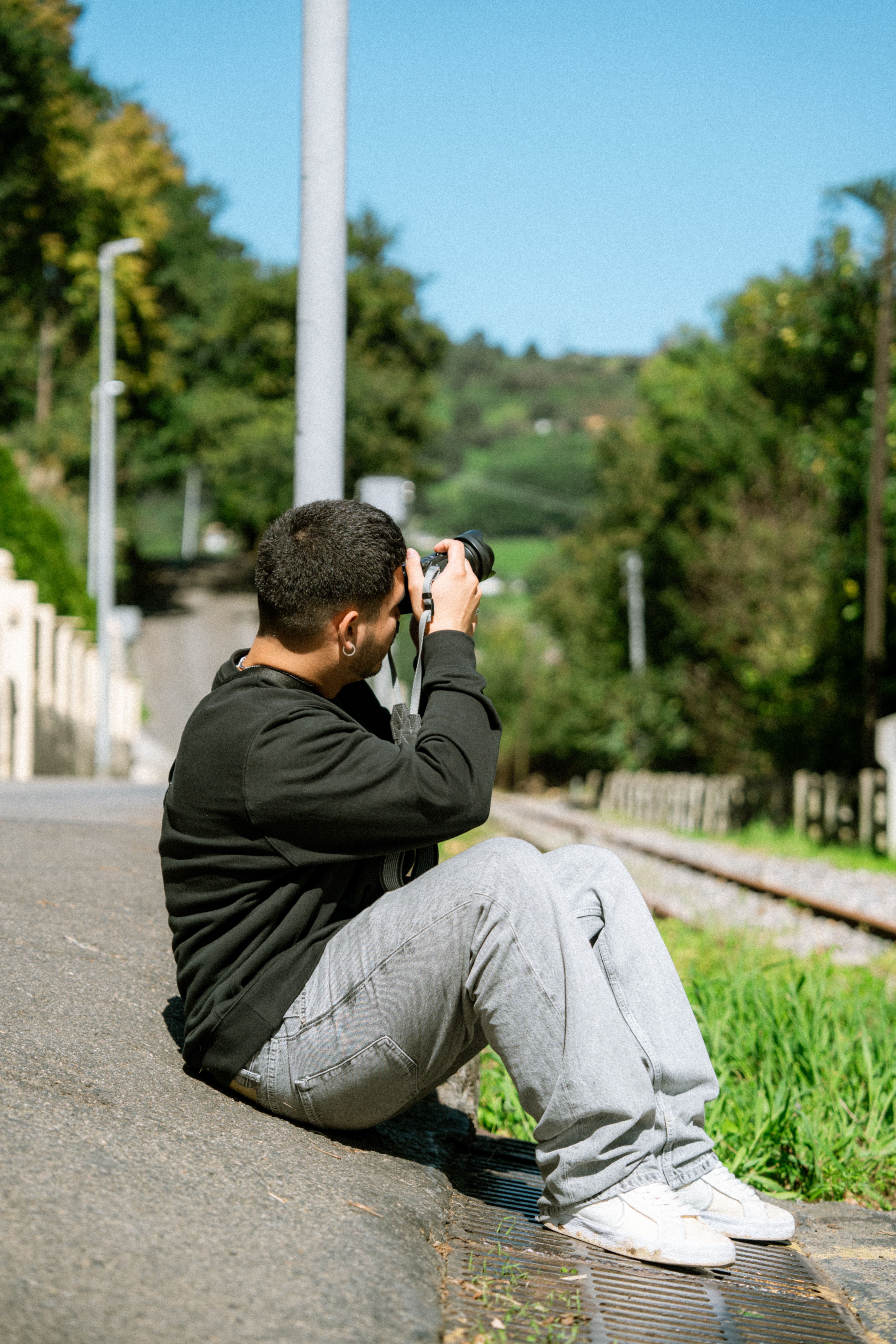 Person sitting on roadside taking pictures with a camera.