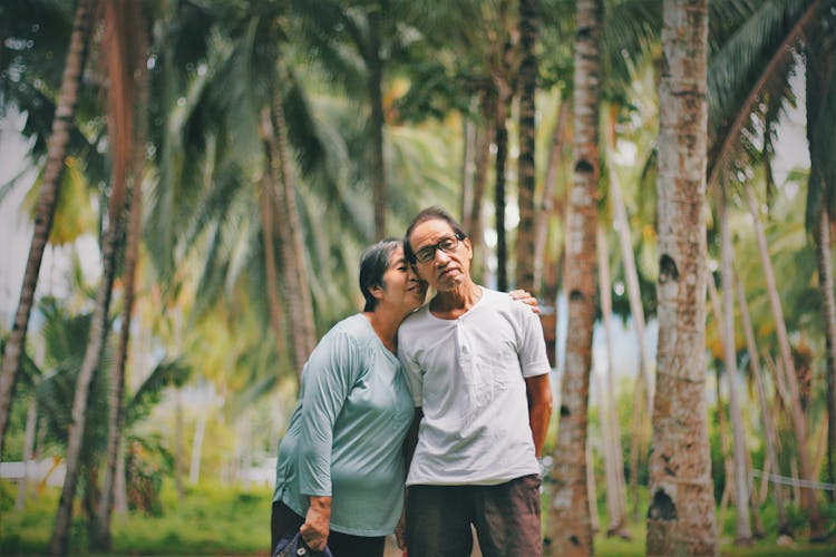 Selective Focus Photo Of Old Couple Standing Together With Trees In The Background