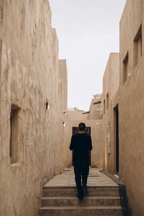 Free Discover the rustic charm of Old Dubai with a lone traveler exploring its narrow alleys at sunset. Stock Photo