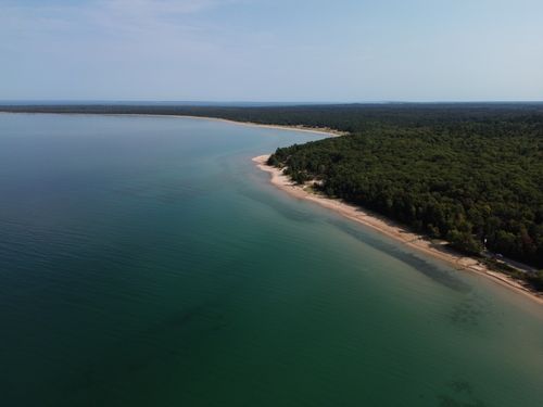 Free Aerial view of pristine sandy beach surrounded by lush green forest in Bliss, Michigan. Stock Photo