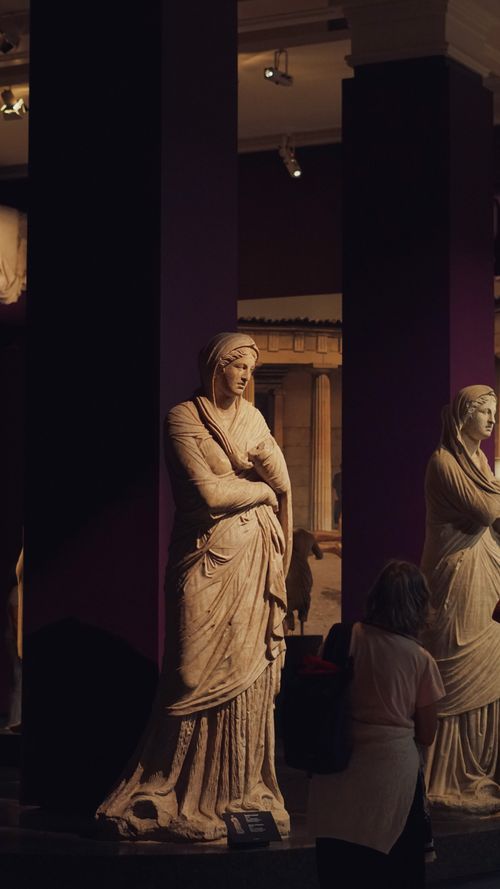 Free Elegant marble statues in a museum setting with warm lighting and visitors. Stock Photo