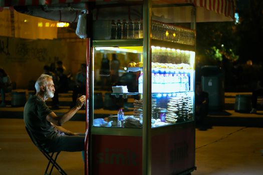 Street vendor selling snacks at night in illuminated booth.