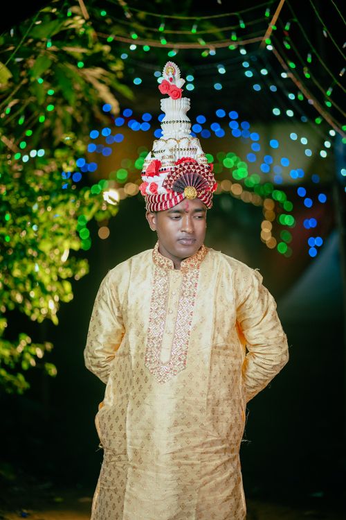Free A Bengali groom in traditional attire with a ceremonial topor during a night wedding. Stock Photo