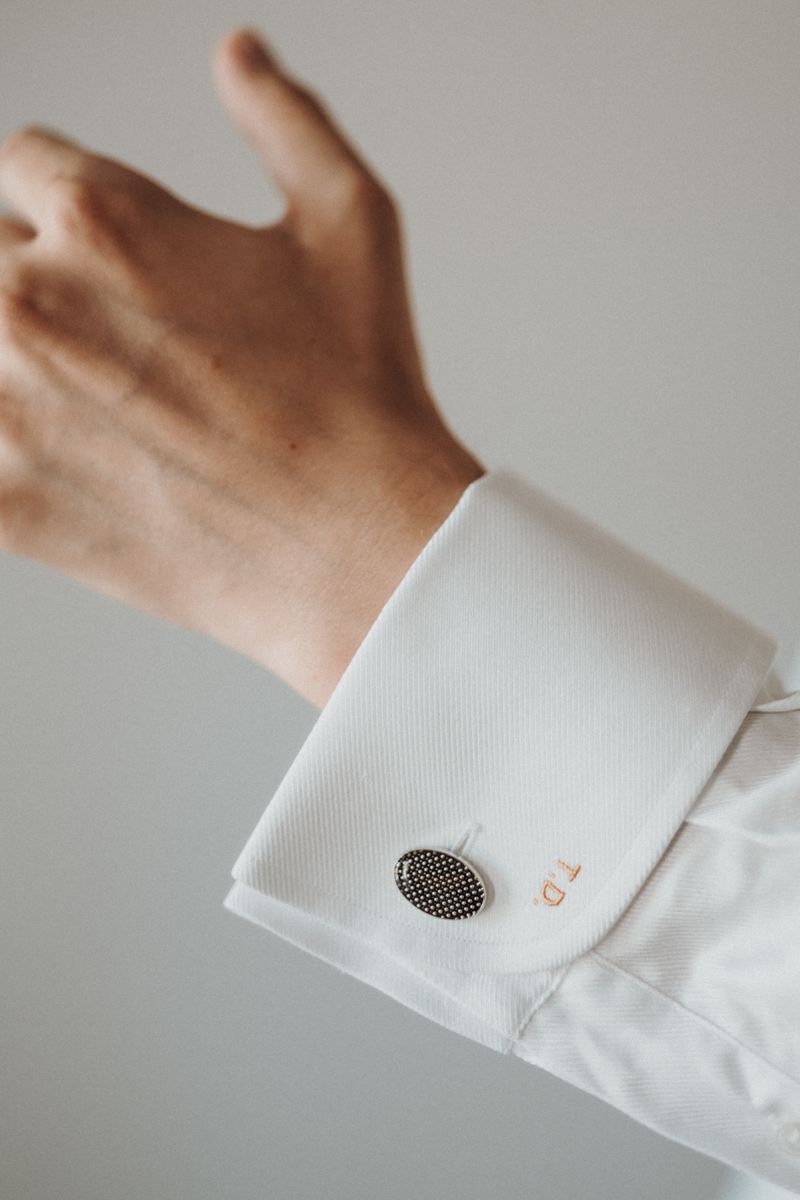 Close-up of a hand with classy cufflinks on a white dress shirt sleeve, showcasing style.