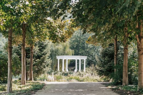 Free Serene forest pathway leading to a picturesque white pavilion in a lush garden. Stock Photo