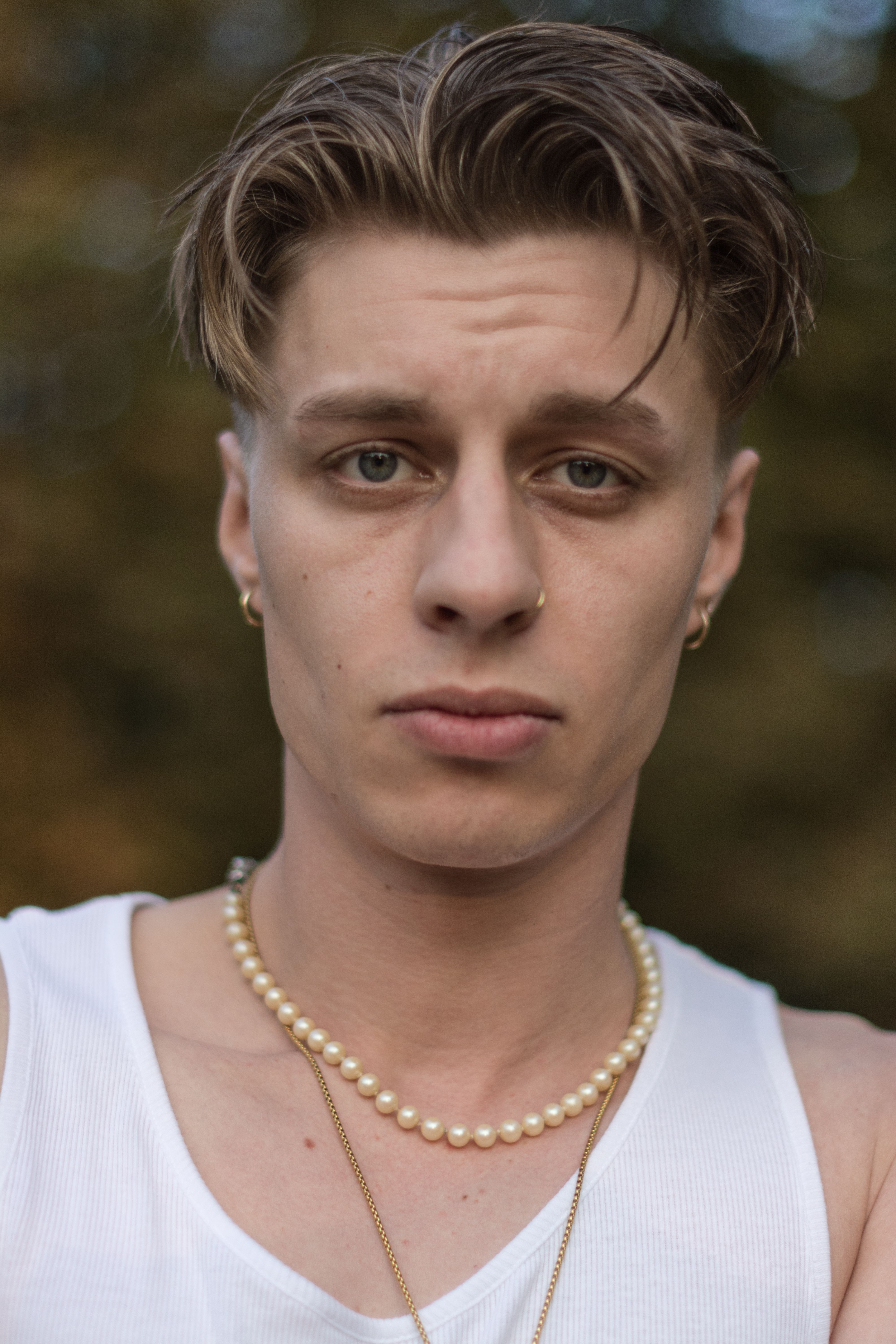 Close-up portrait of a young man wearing a pearl necklace outdoors.