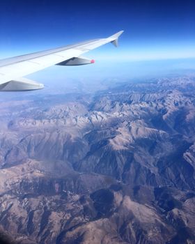 Stunning view of European mountain range from an airplane window in clear blue sky.