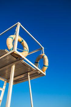 Old lifeguard stand with lifebuoys against clear blue sky.