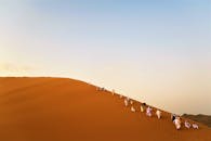 一群成年人在晴朗的天空下攀登沙特阿拉伯贝迪尔沙漠的一座大沙丘