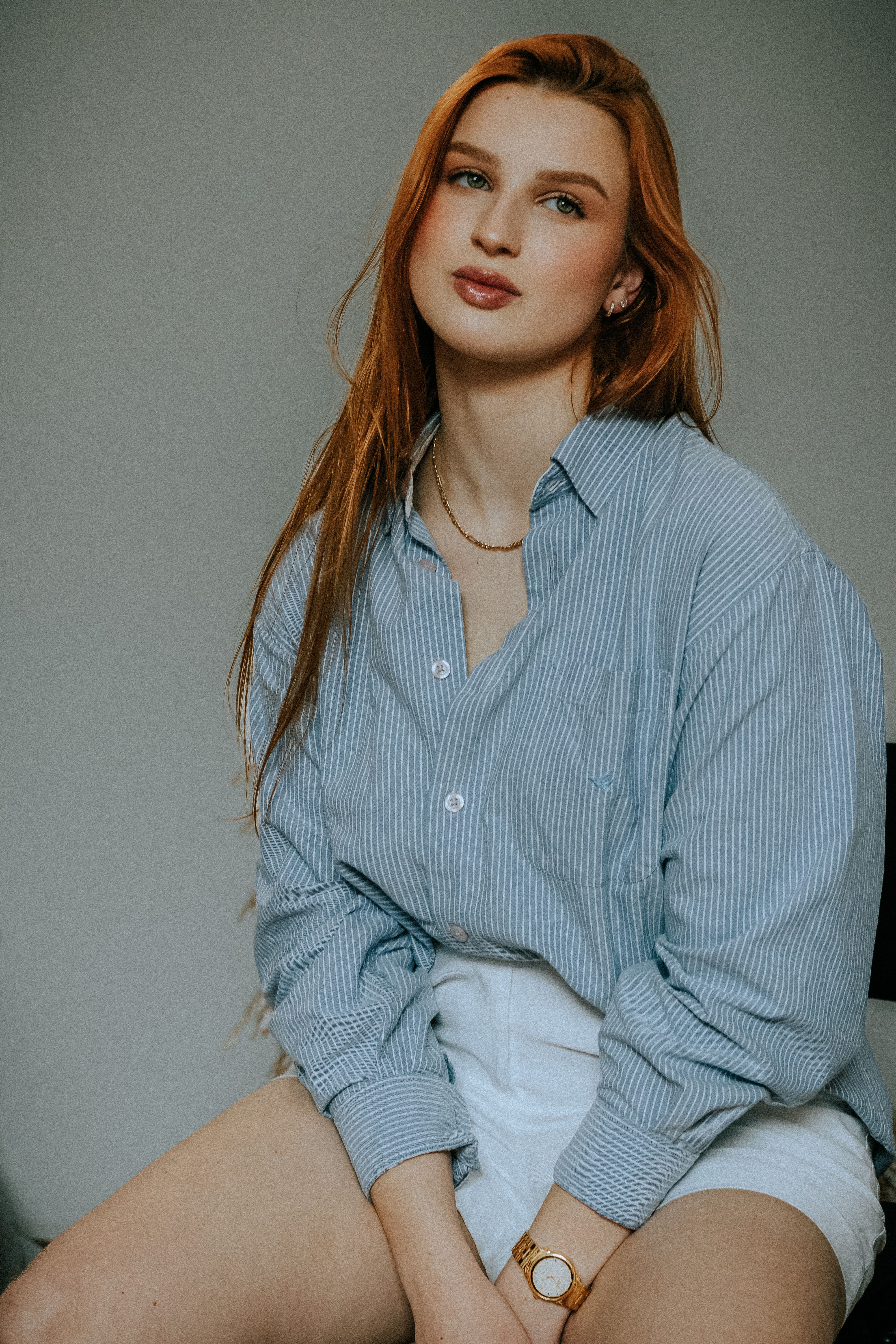 Charming young woman in a casual outfit sits indoors, posing naturally.