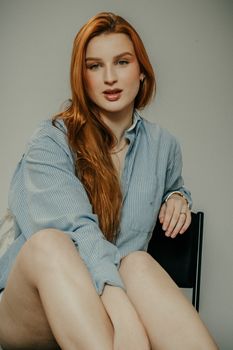 Casual portrait of a relaxed young woman with red hair in a striped shirt indoors.