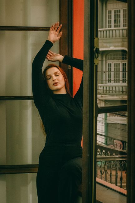 Woman in elegant pose by urban window, embracing peaceful ambiance.