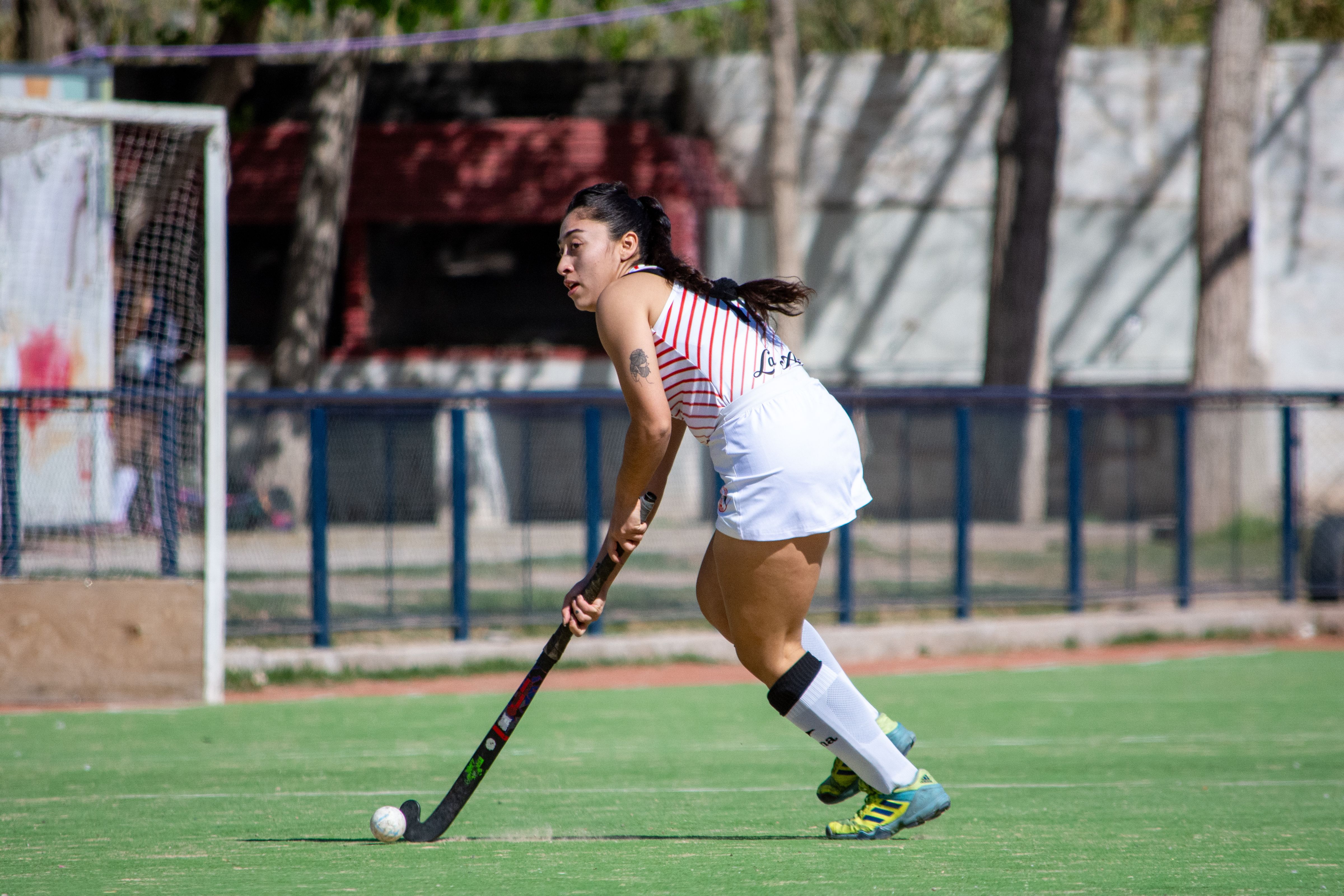 Young woman playing field hockey on a sunny day at an outdoor field.