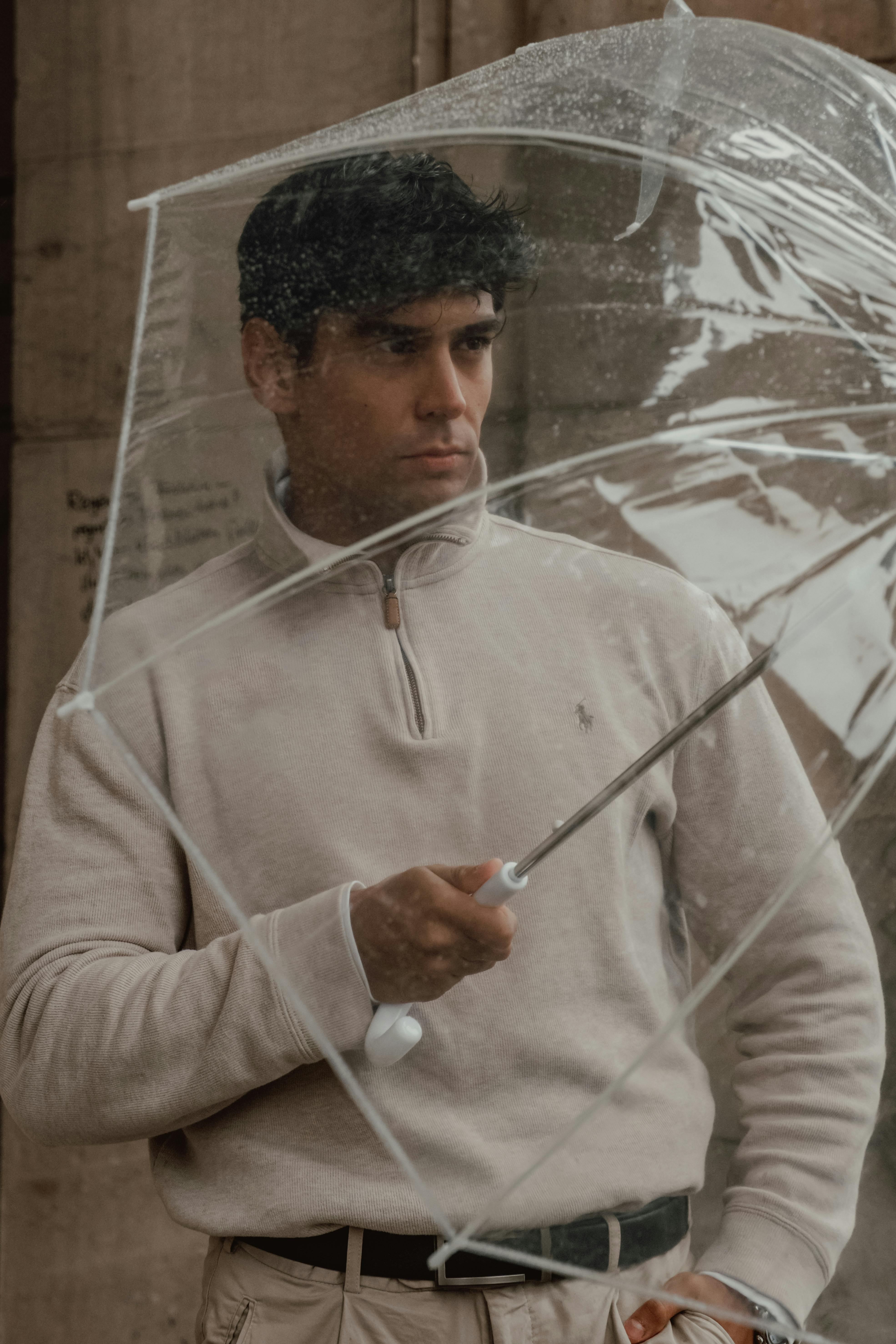 A man holding a clear umbrella, standing outside on a rainy day.