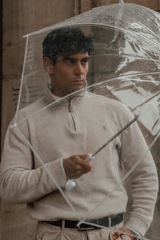 A man holding a clear umbrella, standing outside on a rainy day.