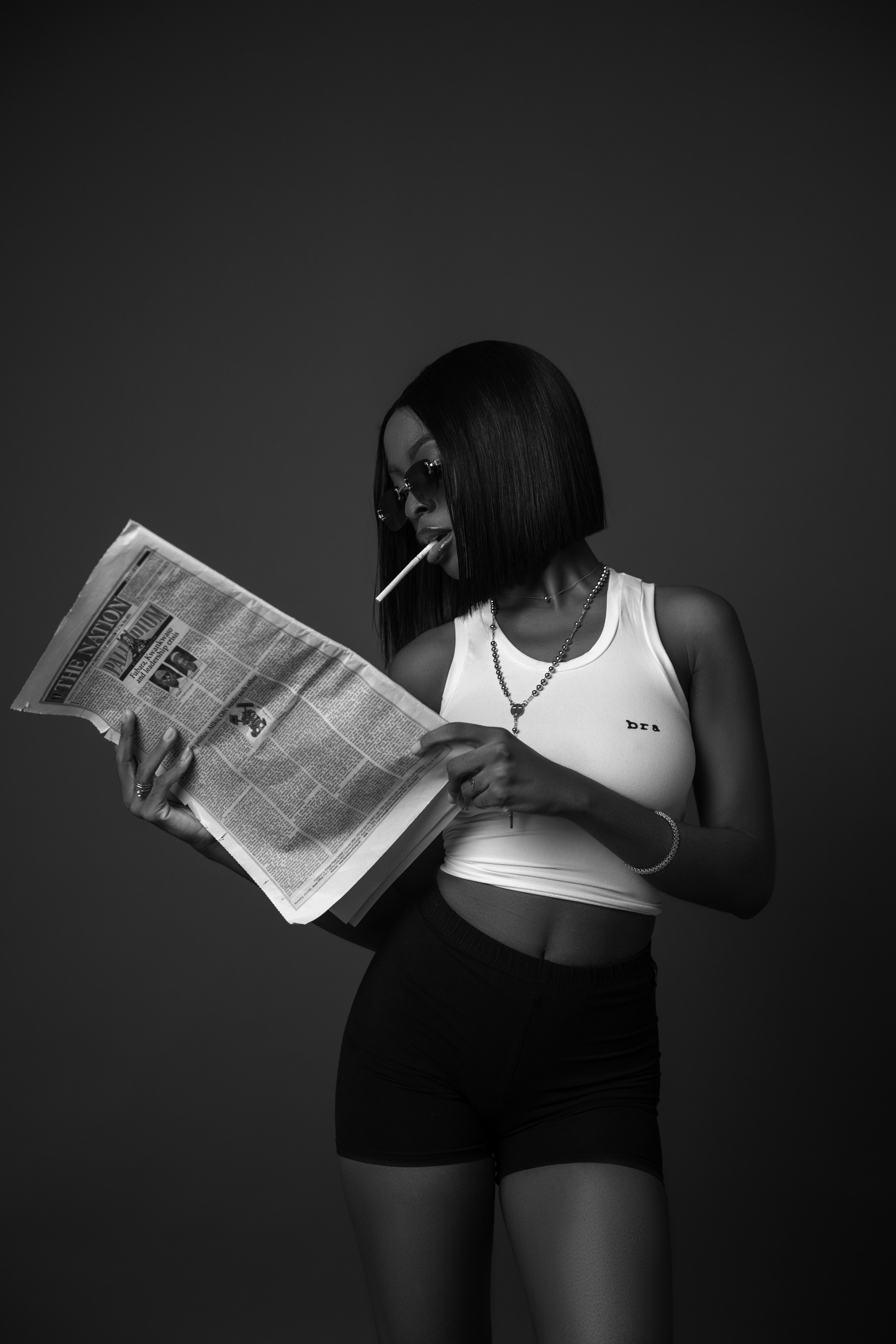 Chic woman with sunglasses reading a newspaper in monochrome.