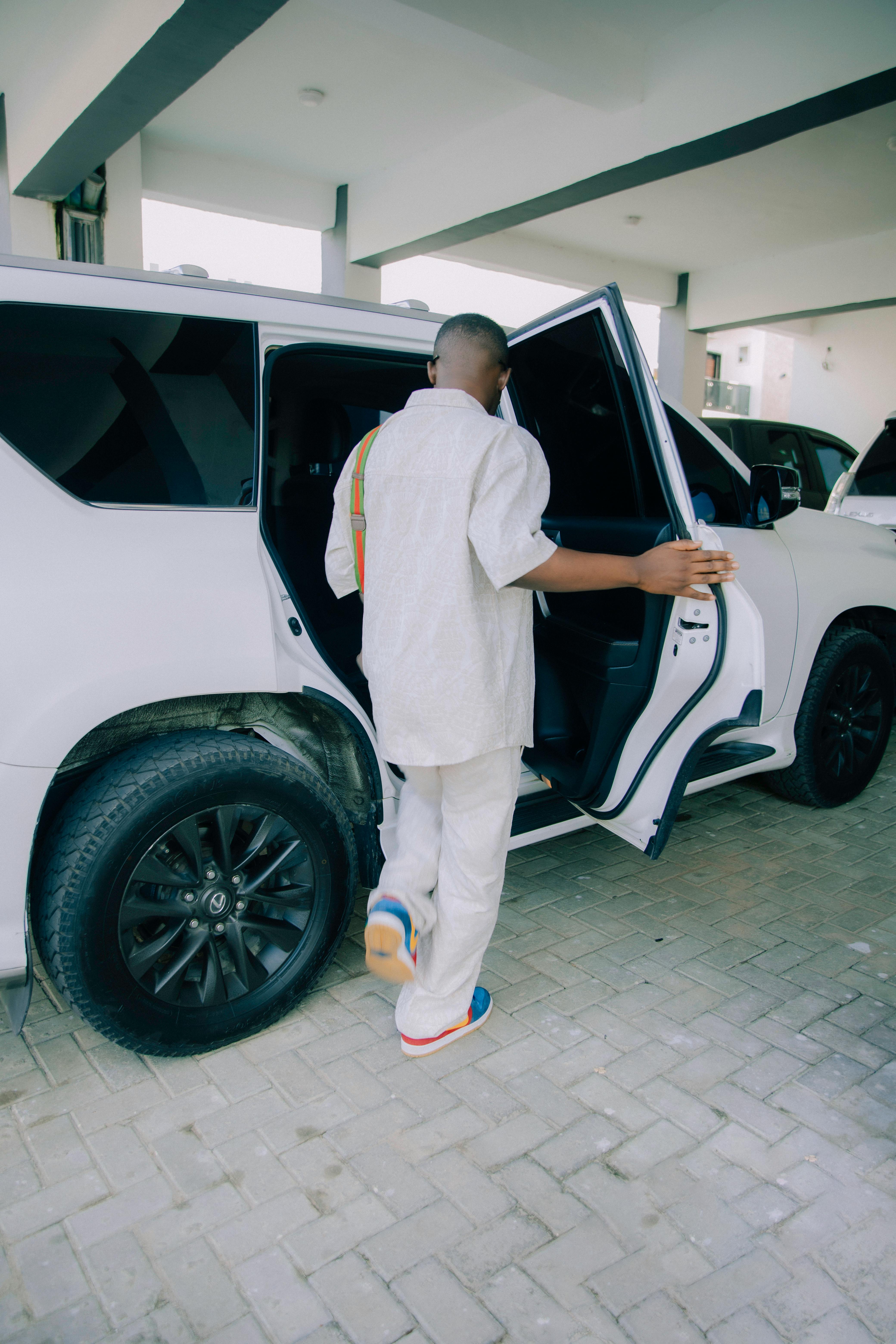 Free Man in fashionable attire getting into a white SUV under a sleek building structure. Stock Photo