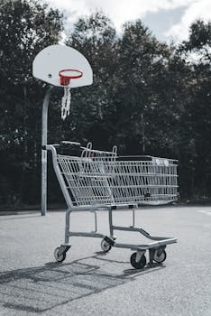 An empty shopping cart on a basketball court with a hoop in the background outdoors.