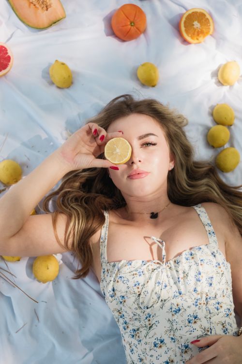 Free Woman lying on a picnic blanket surrounded by lemons and fruits outdoors. Stock Photo