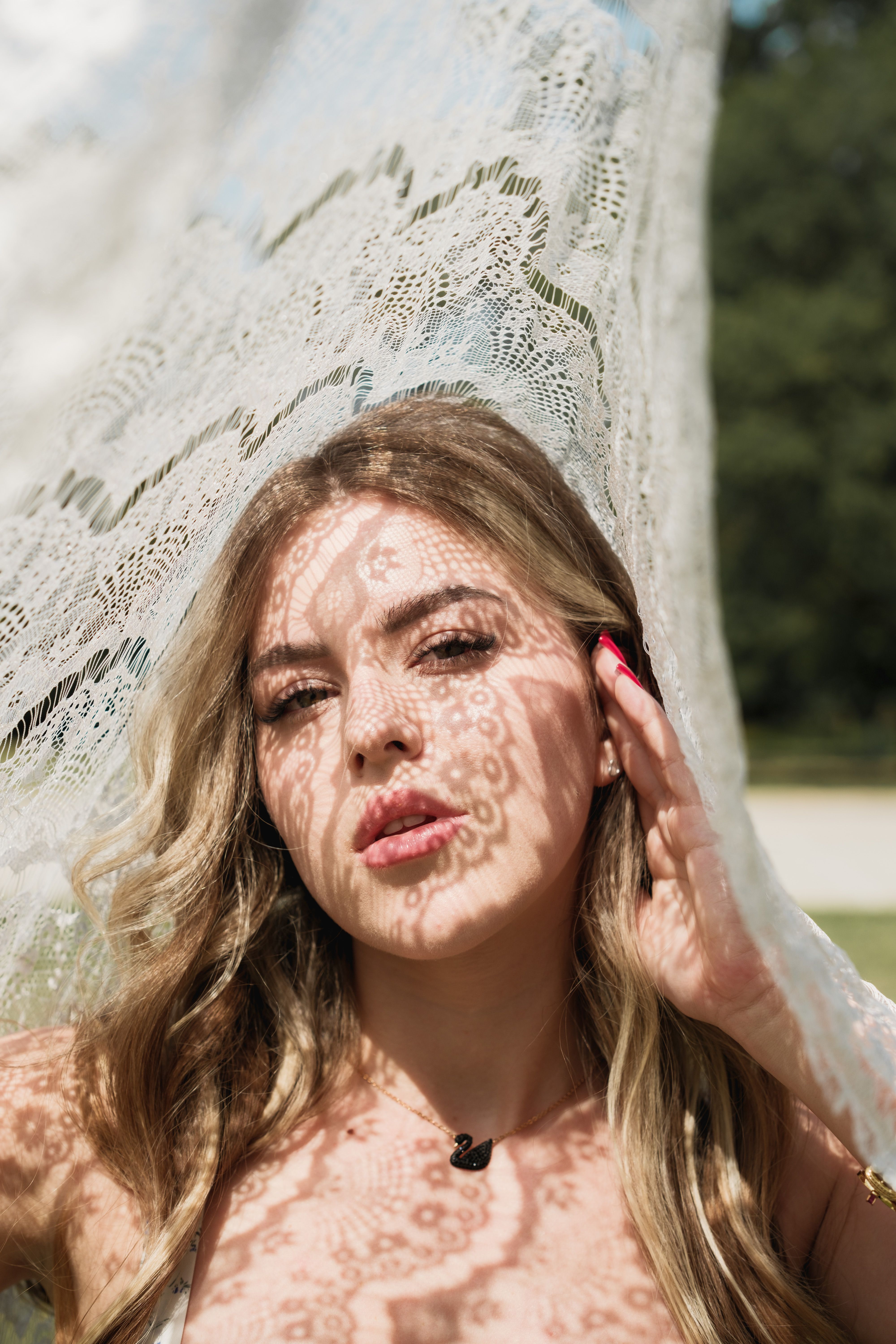 Portrait of a woman with lace shadows on her face in bright sunlight.