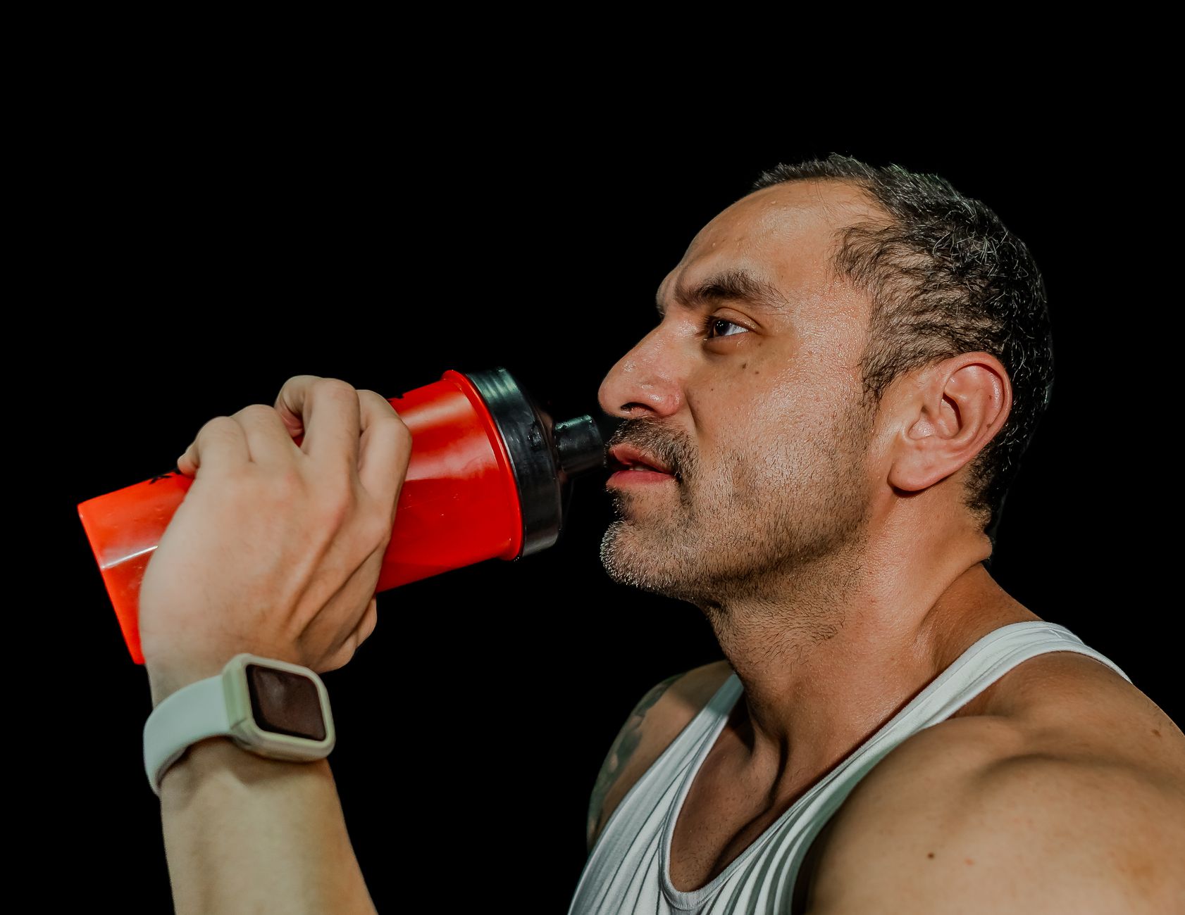 地中海飲食與健美飲食比較:原則、差異與實用選擇 Fit adult male drinking from shaker bottle, fitness focus, black background.