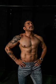 A muscular tattooed man standing confidently in a gym environment. Fitness and strength inspiration.