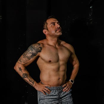 Fit man with tattoos confidently posing in a gym environment.