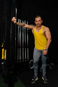 Fit man posing confidently in a gym with weights and equipment, showcasing strength and fitness.