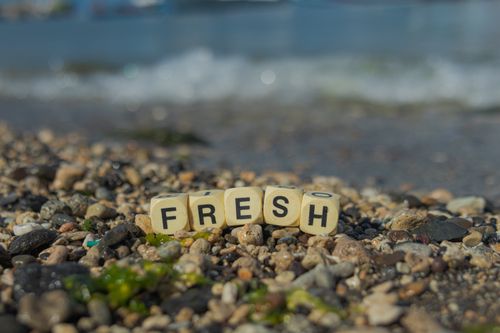 Free A close-up of a pebble beach with the word 'FRESH' spelled out in wooden blocks. Stock Photo