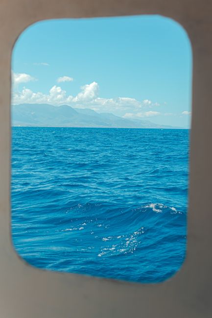 Scenic ocean view through a ship porthole, featuring waves and distant mountains.