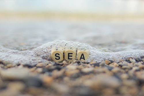 Free Close-up of alphabet cubes spelling 'SEA' amidst bubbles on a pebble beach. Stock Photo