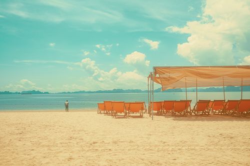 Free Relaxing empty beach with sun loungers and a man in the distance. Stock Photo