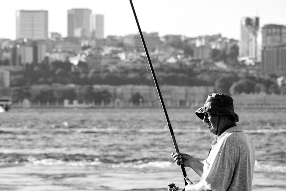 A fisherman in Istanbul city casting a line with the skyline as a backdrop.