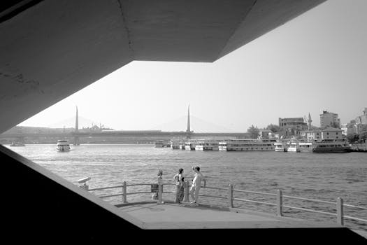 Black and white photo of people on Galata Bridge in Istanbul with urban skyline.