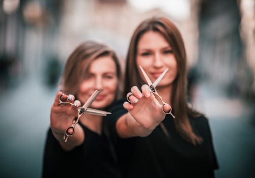 Two female hairdressers showcasing scissors in a stylish outdoor setting.
