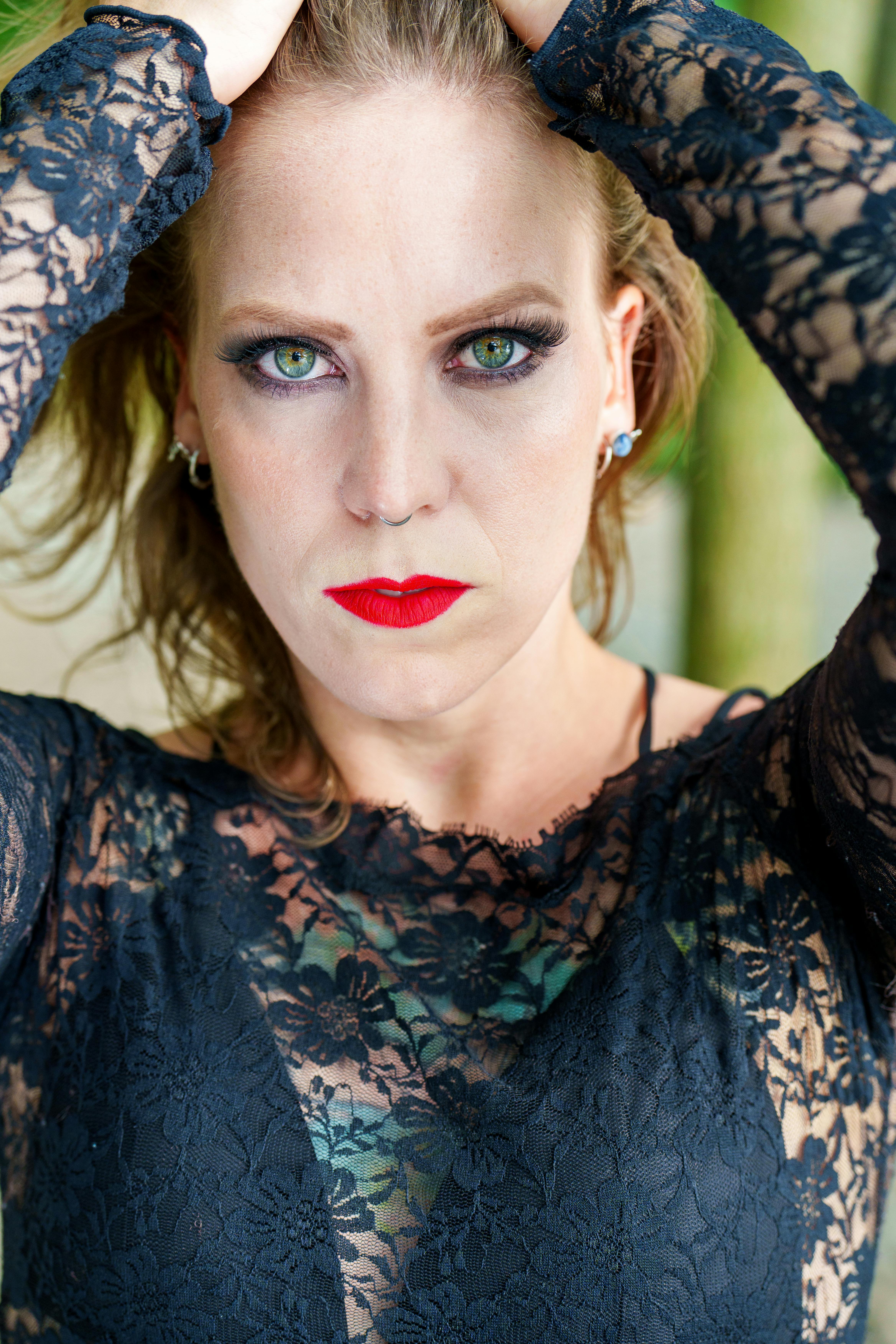 Close-up of a woman in a lace dress with striking red lipstick outdoors.