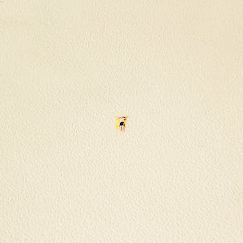 A minimalist aerial shot of a person sunbathing on a sandy beach in Rimini, Italy.