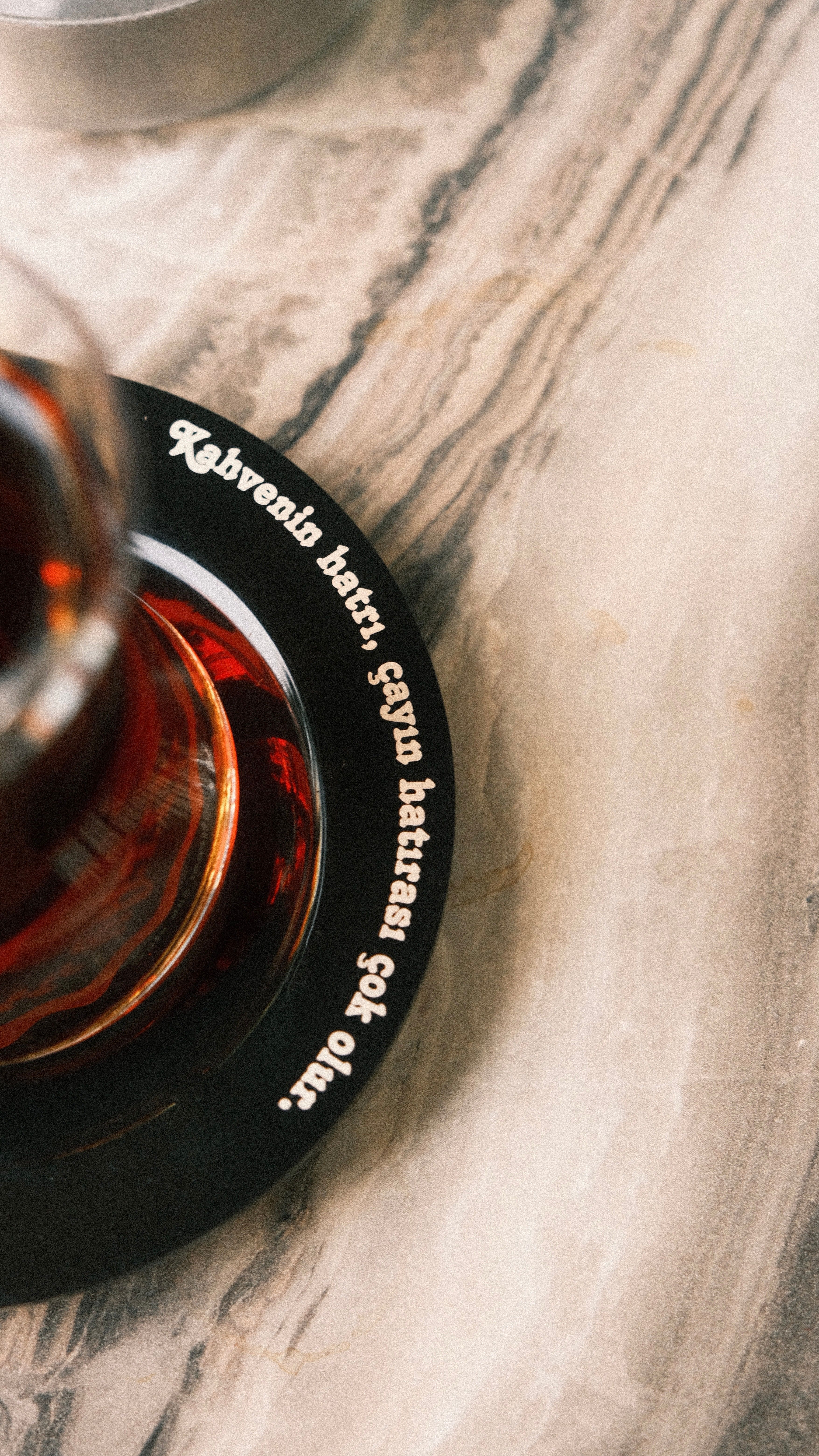 Glass of black tea on a stylish marble table with intriguing text on coaster.