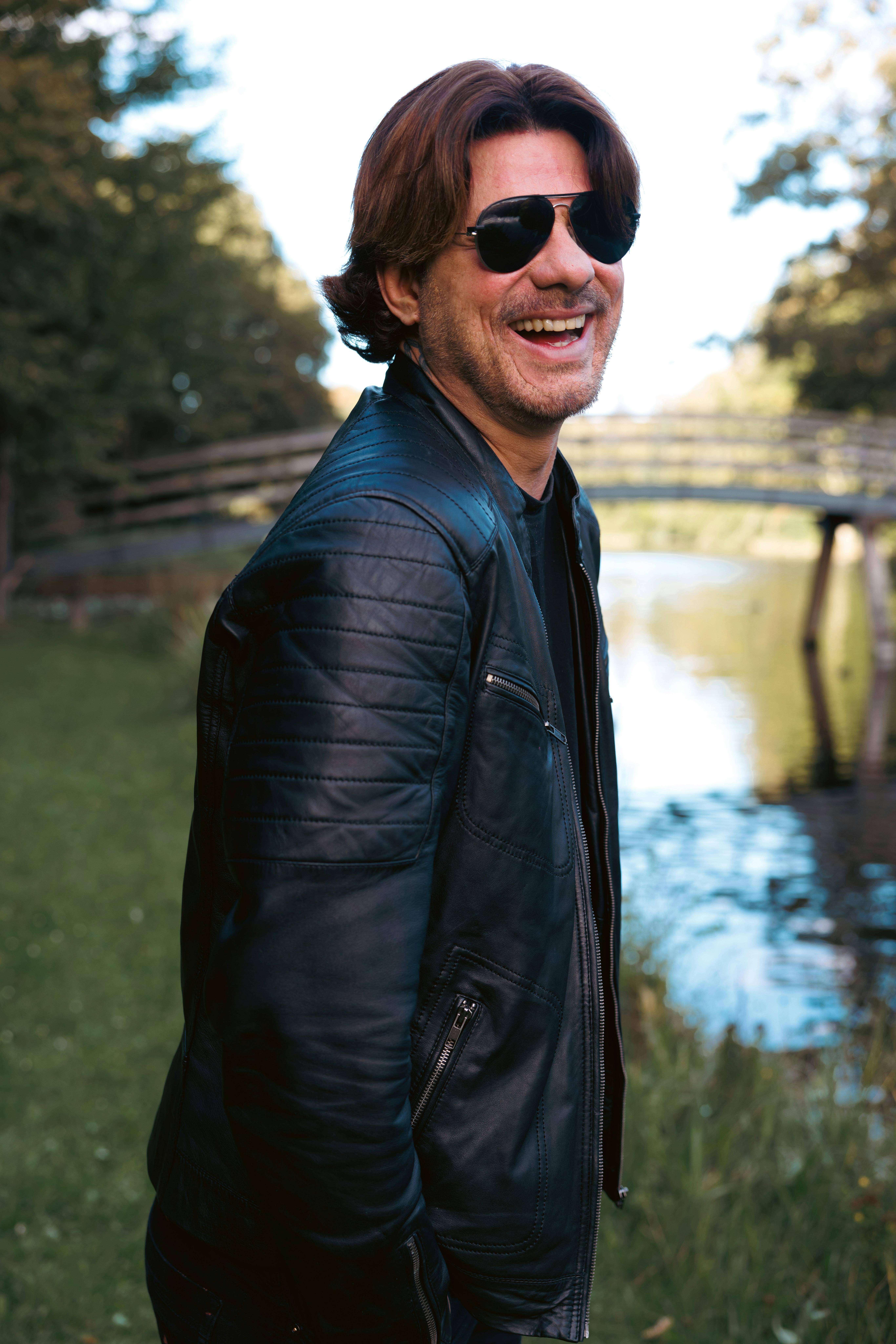 Candid shot of a man in a leather jacket smiling by a river.