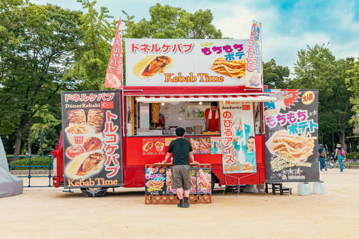 Colorful food stall selling kebabs in a park setting with vibrant signage and an engaging atmosphere.