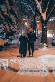 A couple walks under snow-covered trees on a winter night in Konya, Türkiye.