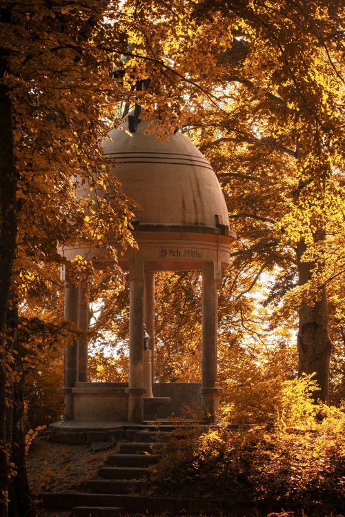 Free A historic stone pavilion surrounded by vibrant autumn foliage in a tranquil forest setting. Stock Photo