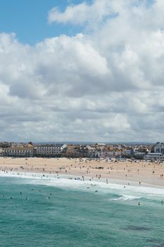 A vibrant summer day at St Ives beach in England, capturing people enjoying the sea and sand under a cloudy sky.